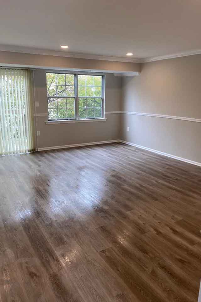 Spacious living room with large window, wood flooring, and recessed lighting.