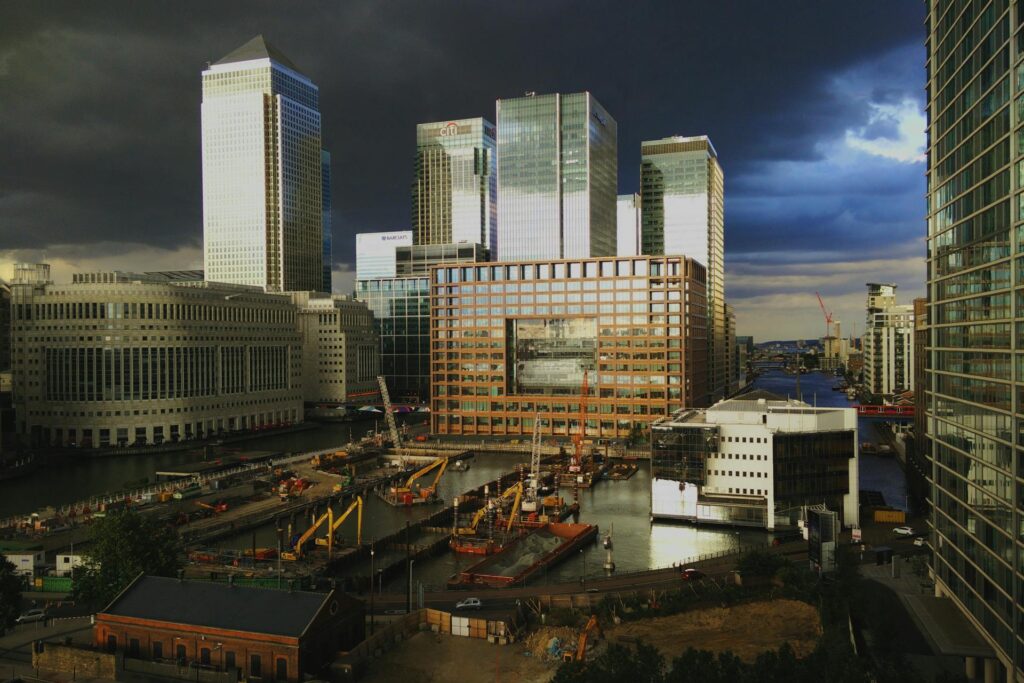 Modern cityscape with tall skyscrapers, construction site, and dramatic cloudy sky.
