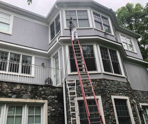 Worker on ladder painting exterior of a gray modern house.