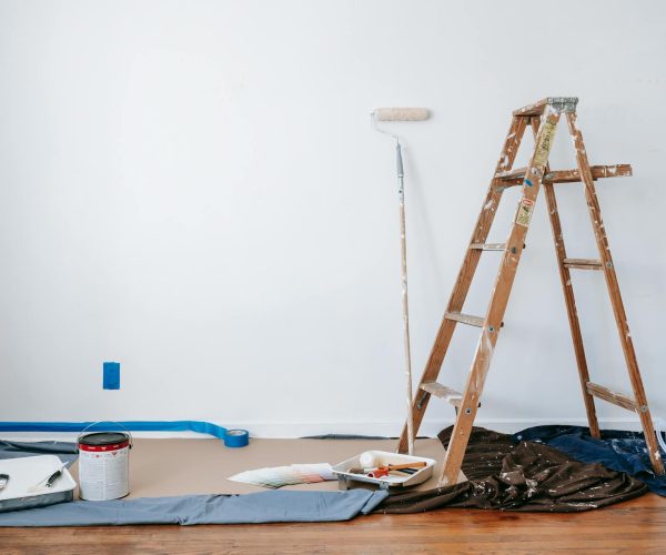 pexels-blue-bird-7218525 Interior painting setup with ladder, roller, and paint cans.