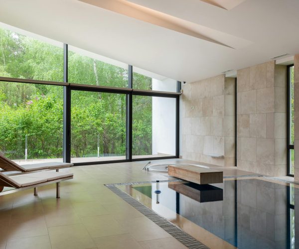 pexels-heyho-6908372 Luxurious indoor pool with loungers and large windows overlooking nature.