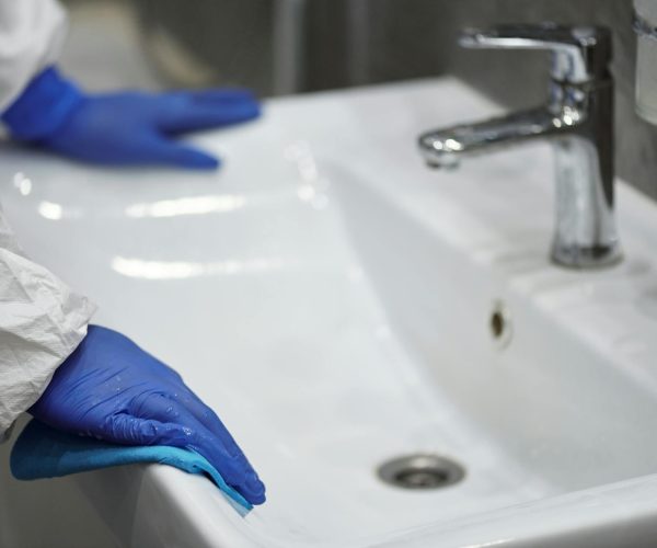 Professional cleaning white sink with blue gloves.